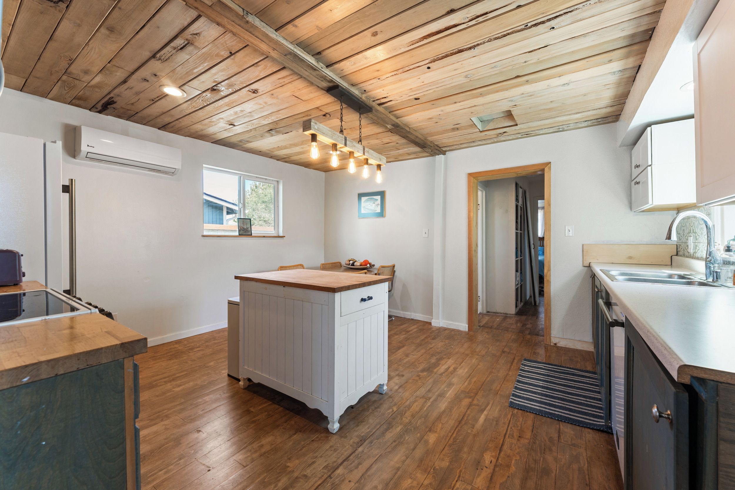 A kitchen with wooden flooring, a central island, and a hanging light fixture.