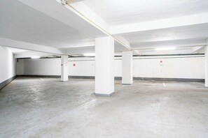 A parking garage with white walls and columns, concrete floor, and emergency exit signs. - Algarve Oceanfront Luxury Penthouse (Armação de Pêra)