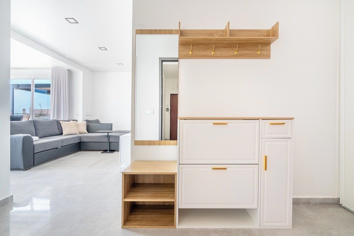 A modern living room with a grey sectional sofa, a wooden coffee table, and a white wardrobe with drawers.