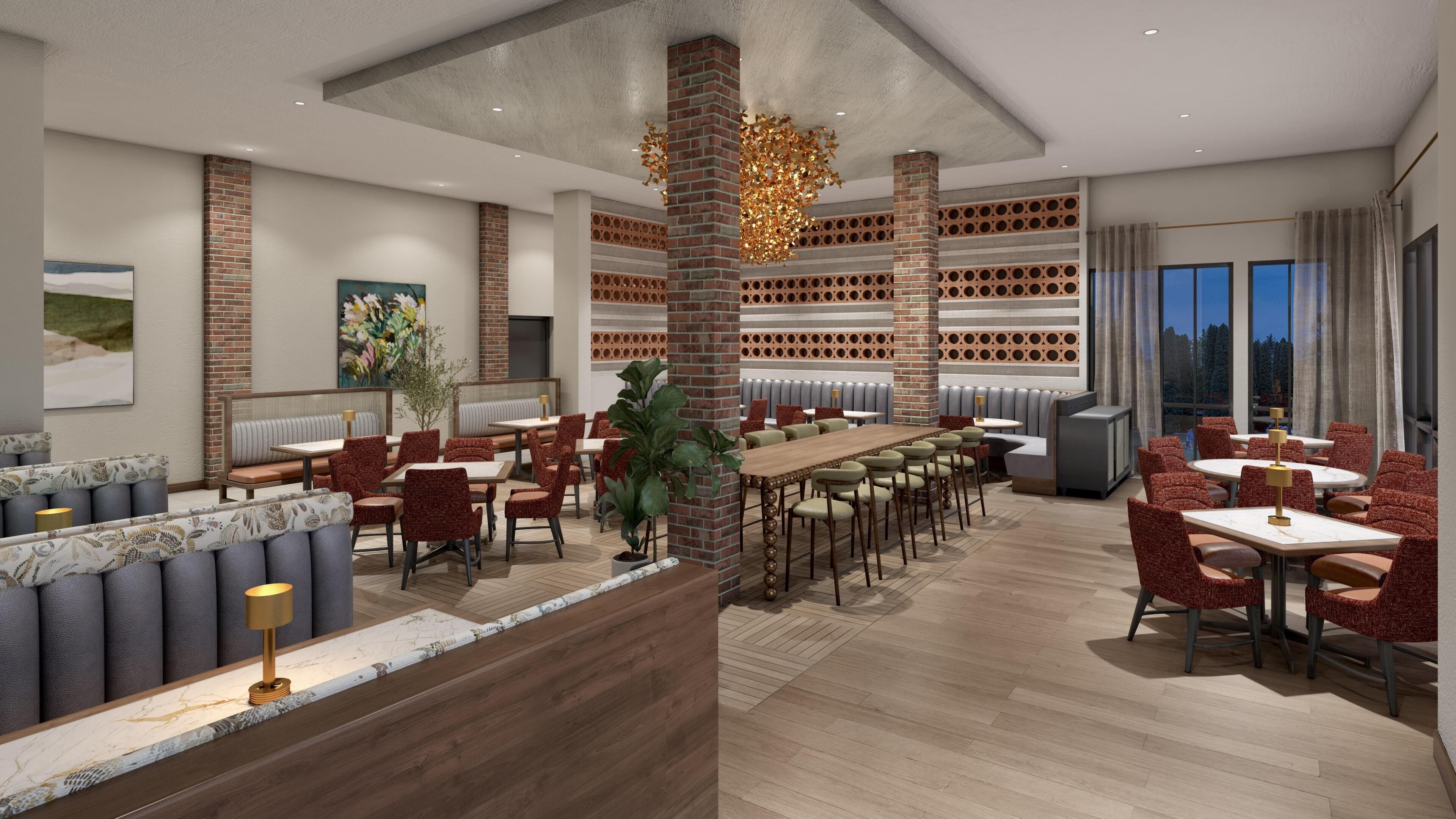 A modern restaurant with a long wooden table and red upholstered chairs, brick pillars, and a large window with a view.
