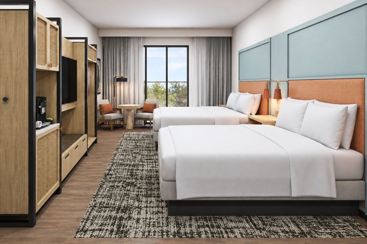 Una habitación de hotel con dos camas, un escritorio, una silla, un televisor y una ventana con cortinas.