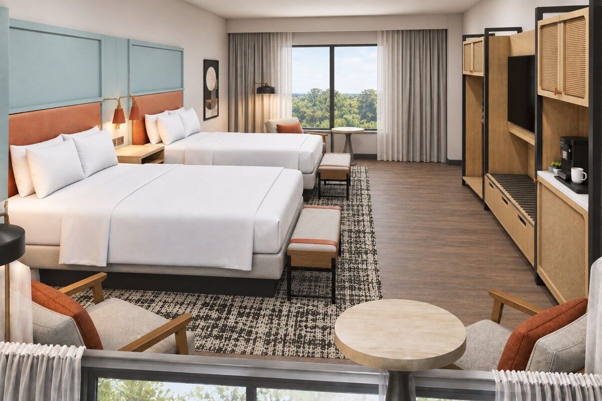 Habitación de hotel con dos camas, un escritorio, una silla, una mesa redonda y vistas al exterior.