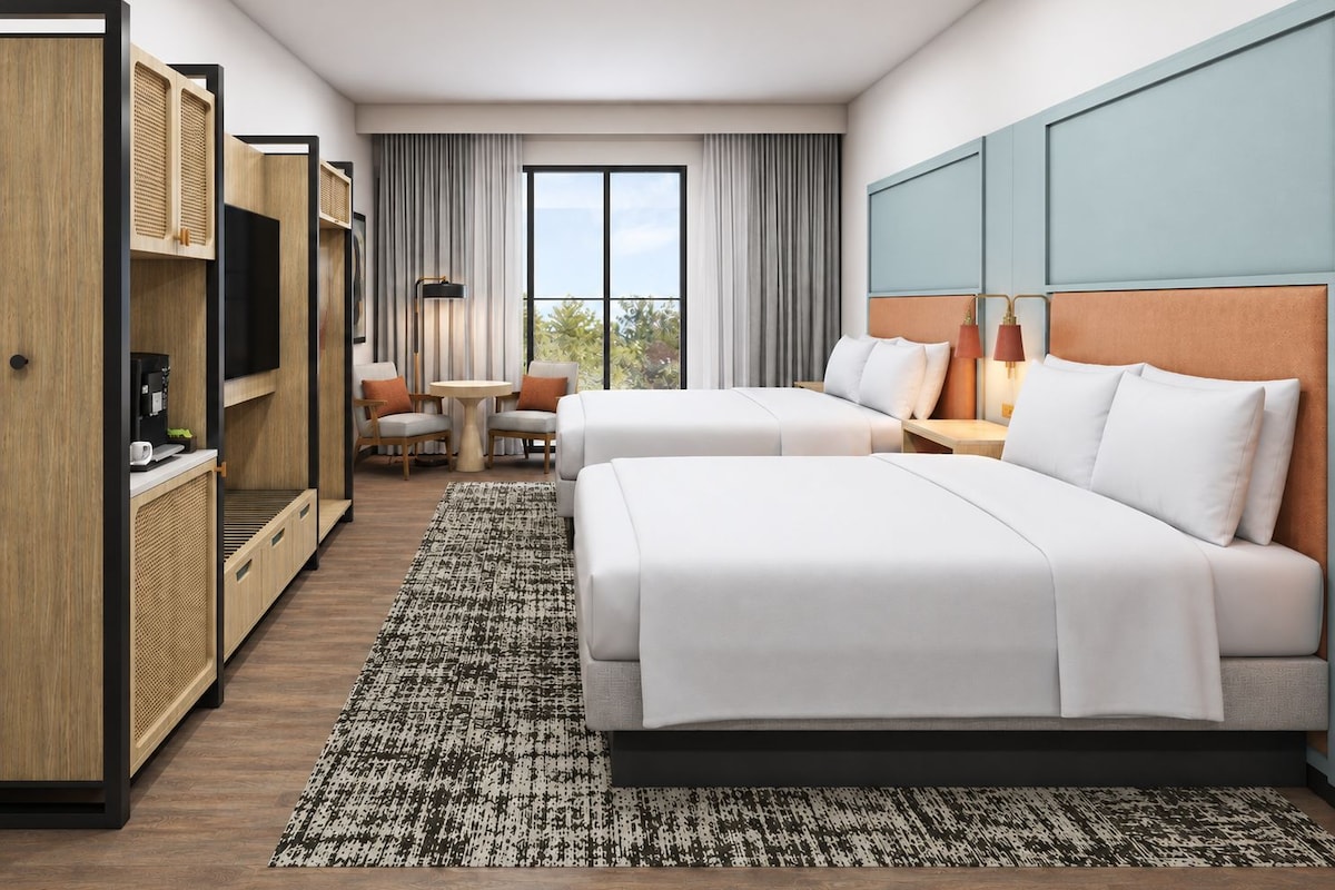 Una habitación de hotel con dos camas, un escritorio, una silla, un televisor y una ventana con cortinas.