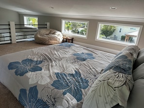 Een slaapkamer met een groot bed, een zachte kruppelstoel en uitzicht buiten door twee ramen.