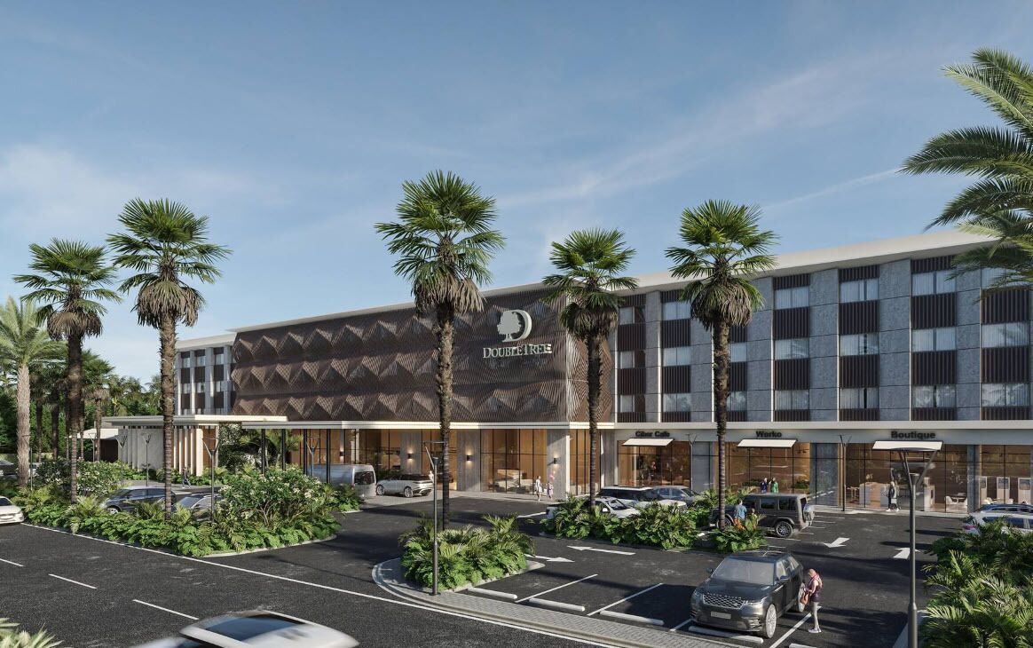 Un hôtel moderne, reconnaissable à son grand panneau « DOUBLE TREE », qui se distingue par sa façade aux lignes géométriques et la présence de palmiers.