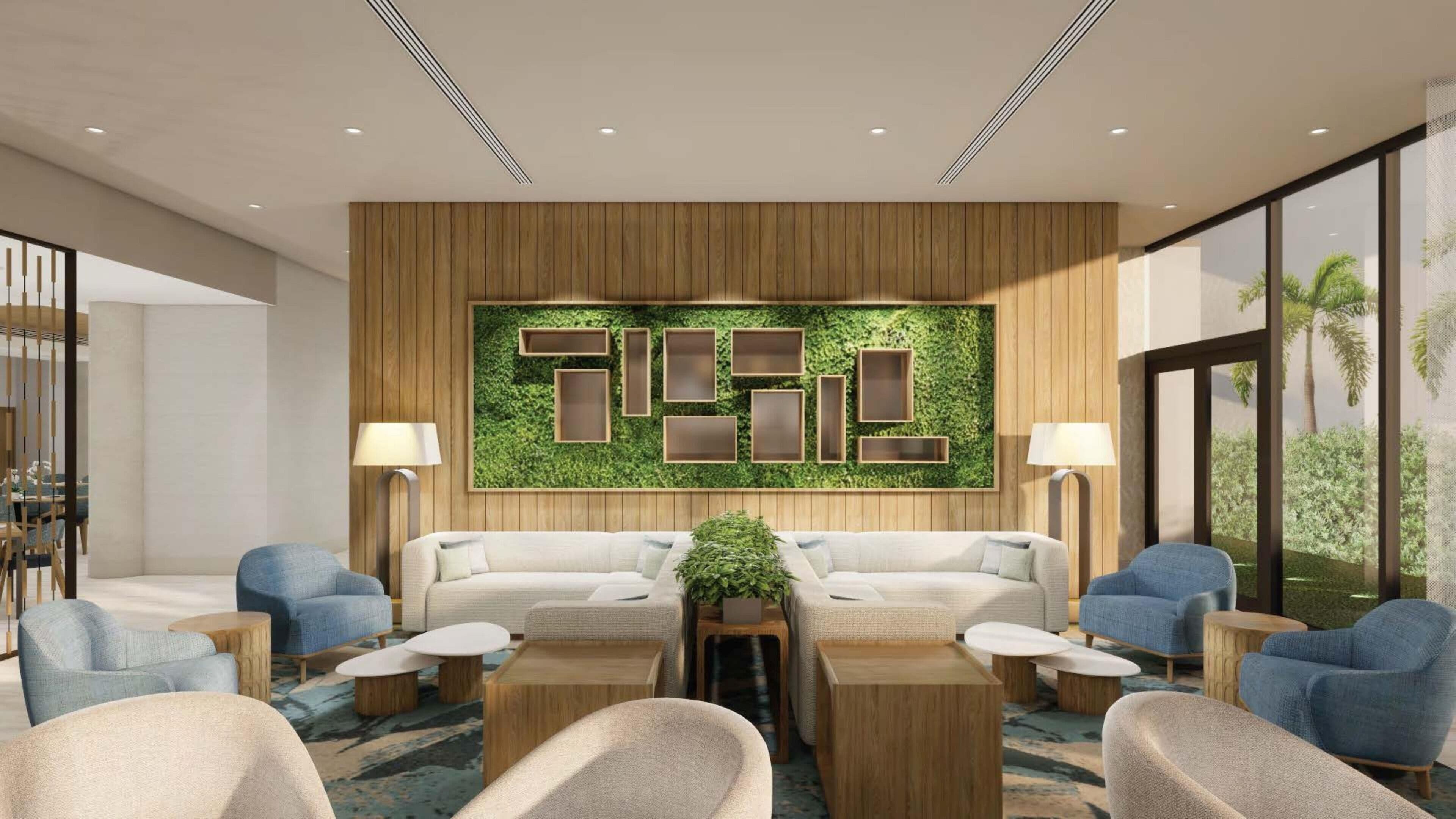 En modern hotellobby med en väggpanel i trä, en grön vägg med inramade bilder och en sittgrupp med soffor och fåtöljer.