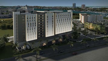 Ett modernt hotell med en central innergård, omgivet av palmer och en småbåtshamn i bakgrunden.