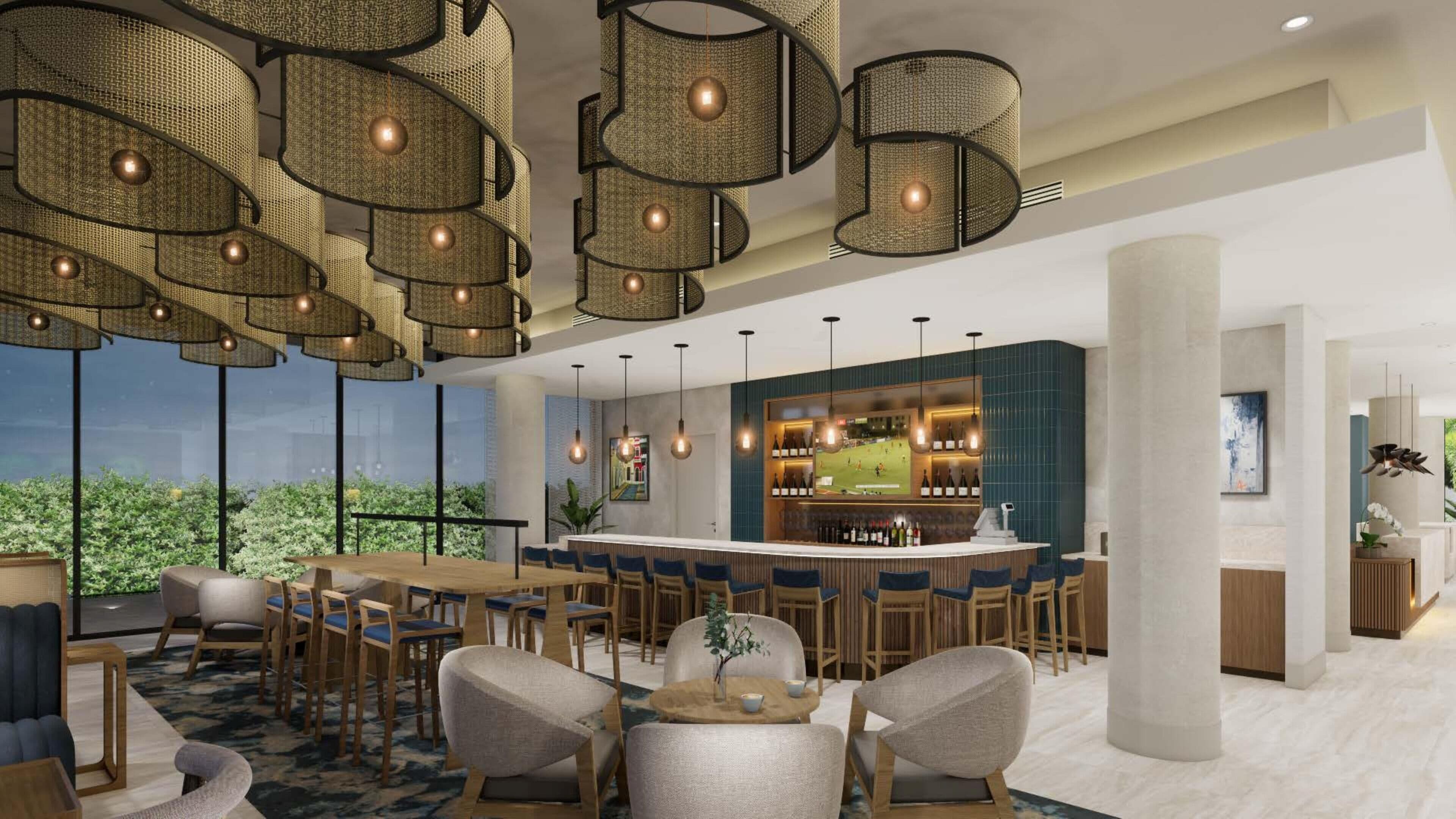 A modern bar area with high ceilings, wicker pendant lighting, and a bar counter with a large screen displaying sports.