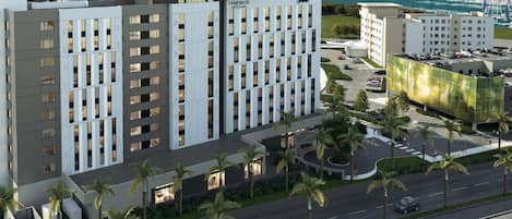A modern hotel with a central courtyard, surrounded by palm trees and a marina in the background.