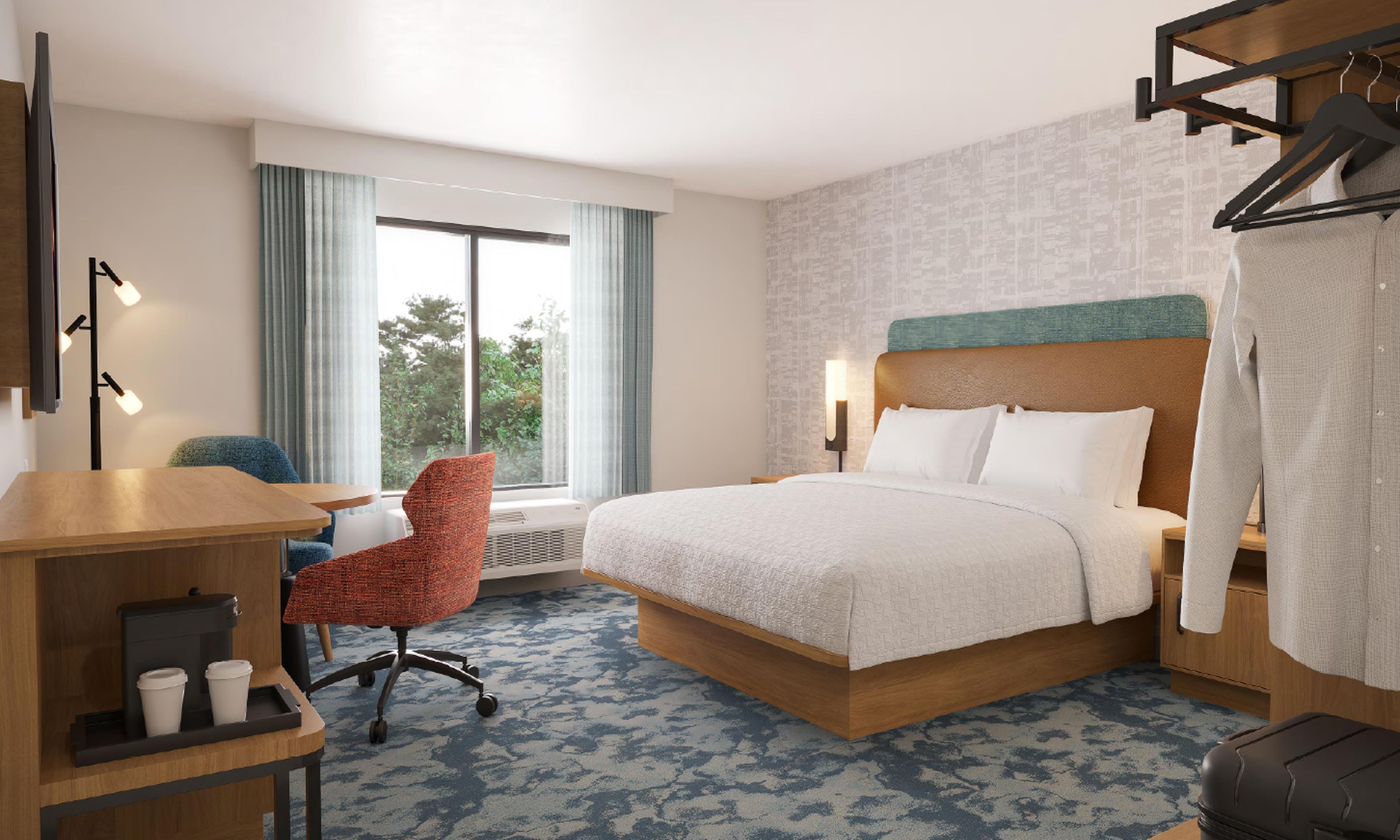 Quarto de hotel com cama, escrivaninha com cafeteira, cadeira, mala e janela com cortinas.