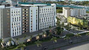 A modern hotel with a central courtyard, surrounded by palm trees and a marina in the background. - Homewood Suites By Hilton San Juan (San Juan)