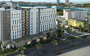 Hotel moderno com um pátio central, rodeado por palmeiras e um porto na distância.
