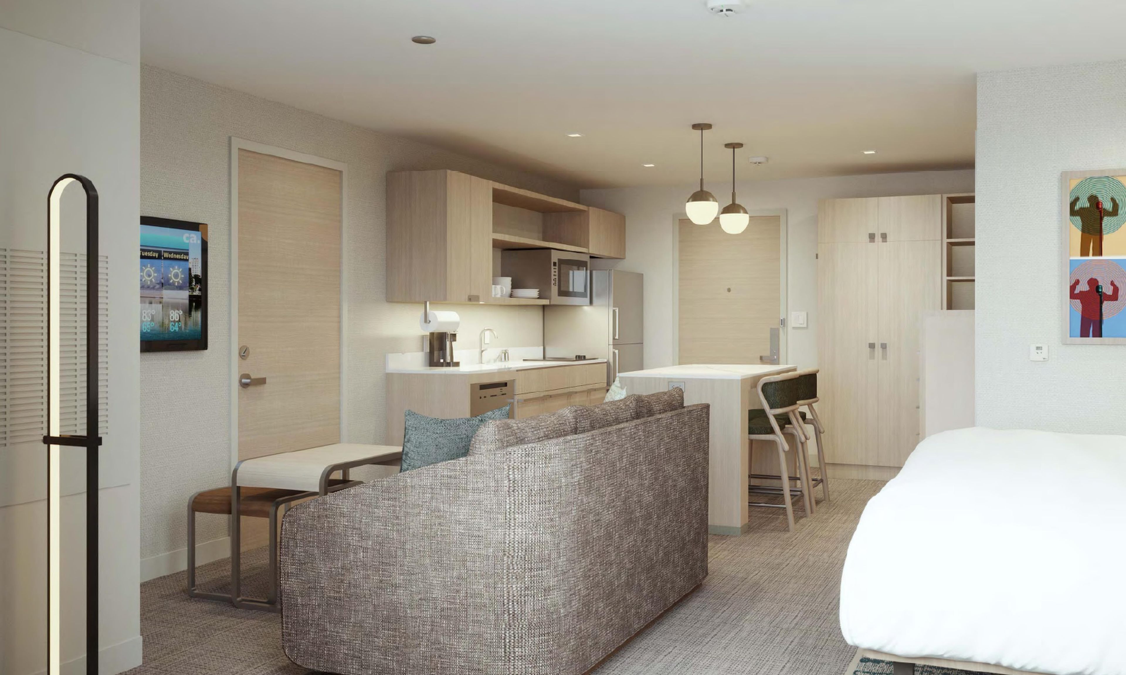 A modern hotel room with a kitchenette, a sofa, a dining area, and a bed.