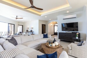A modern living room with a sectional sofa, a coffee table, a TV, and a ceiling fan. - Charming 3-bedroom estate in Osa • Private Pool • 180° Ocean View in Jungle (Puntarenas Province)
