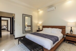 A hotel room with a large bed, bedside lamps, a nightstand, a bench, and a wall-mounted air conditioner. - Charming 3-bedroom estate in Osa • Private Pool • 180° Ocean View in Jungle (Puntarenas Province)
