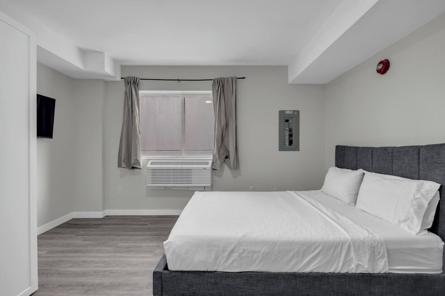 Ein Hotelzimmer mit einem großen Bett, einem fenster mit Vorhängen, einer Wandklimaanlage und einem Rauchmelder.