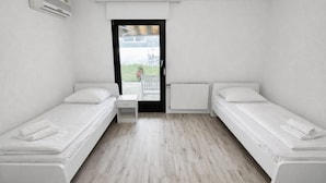 A small, clean room with two single beds, a small table, and a window with a view of the outside. - Frankfurt east Family House (Heusenstamm)