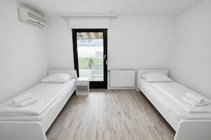 A small, clean room with two single beds, a small table, and a window with a view of the outside. - Frankfurt east Family House (Heusenstamm)