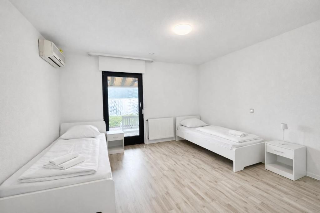 Una habitación pequeña y blanca con dos camas, una ventana y un radiador.