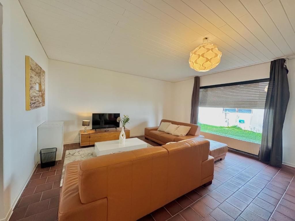 A modern living room with a sofa, a coffee table, a TV, and a window with curtains.