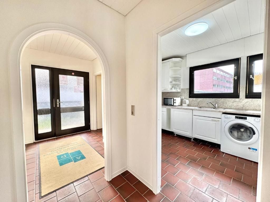 A hallway leading to a kitchen with a washing machine, a door with frosted glass, and a tiled floor.