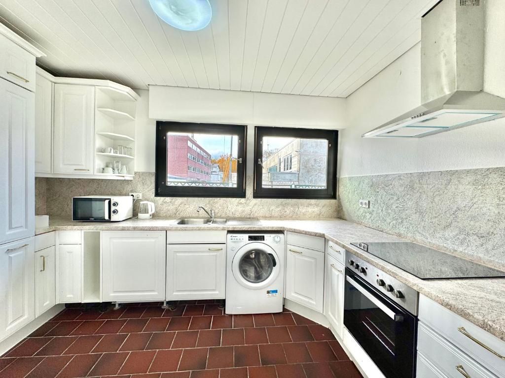 Een kleine keuken met witte kastjes, een wasmachine, een magnetron en een fornuis.
