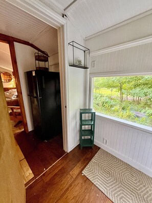 Una stanza con pavimento in legno, un frigorifero nero, uno scaffale verde e una finestra vista verde.