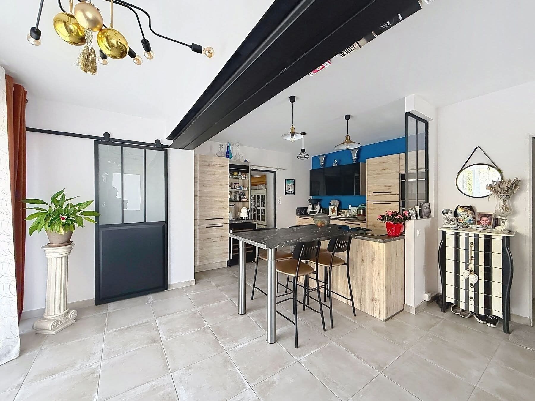 A modern kitchen with a central island, a dining area with chairs, and a sliding glass door leading to another room.