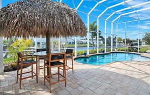 Zona junto a la piscina con un área de estar techada y vista a la pileta.