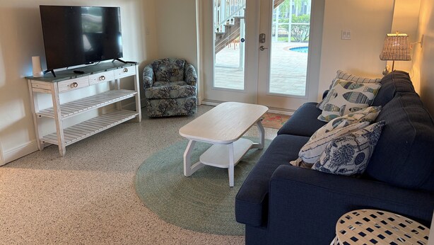 Uma sala de estar com televisão, sofá, mesa de centro e poltrona estampada.