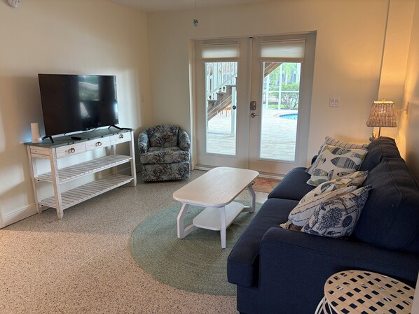 Una sala de estar con televisor, sofá, mesa de centro y sillón estampado.
