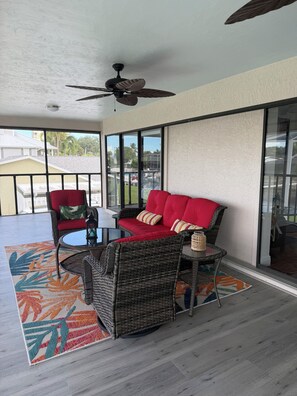 Ein überdachter Patio-Bereich mit Korbmöbeln, einem Deckenventilator und Blick auf die Nachbarschaft.