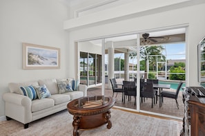 A spacious living room with a white sofa, a round wooden coffee table, and a dining area with chairs and a table. - Heated Pool home with Amazing Gulf Access in Southeast Cape! (Cape Coral)