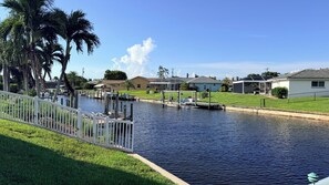 A waterfront property with a dock, a grassy area, and houses in the background. - Heated Pool home with Amazing Gulf Access in Southeast Cape! (Cape Coral)
