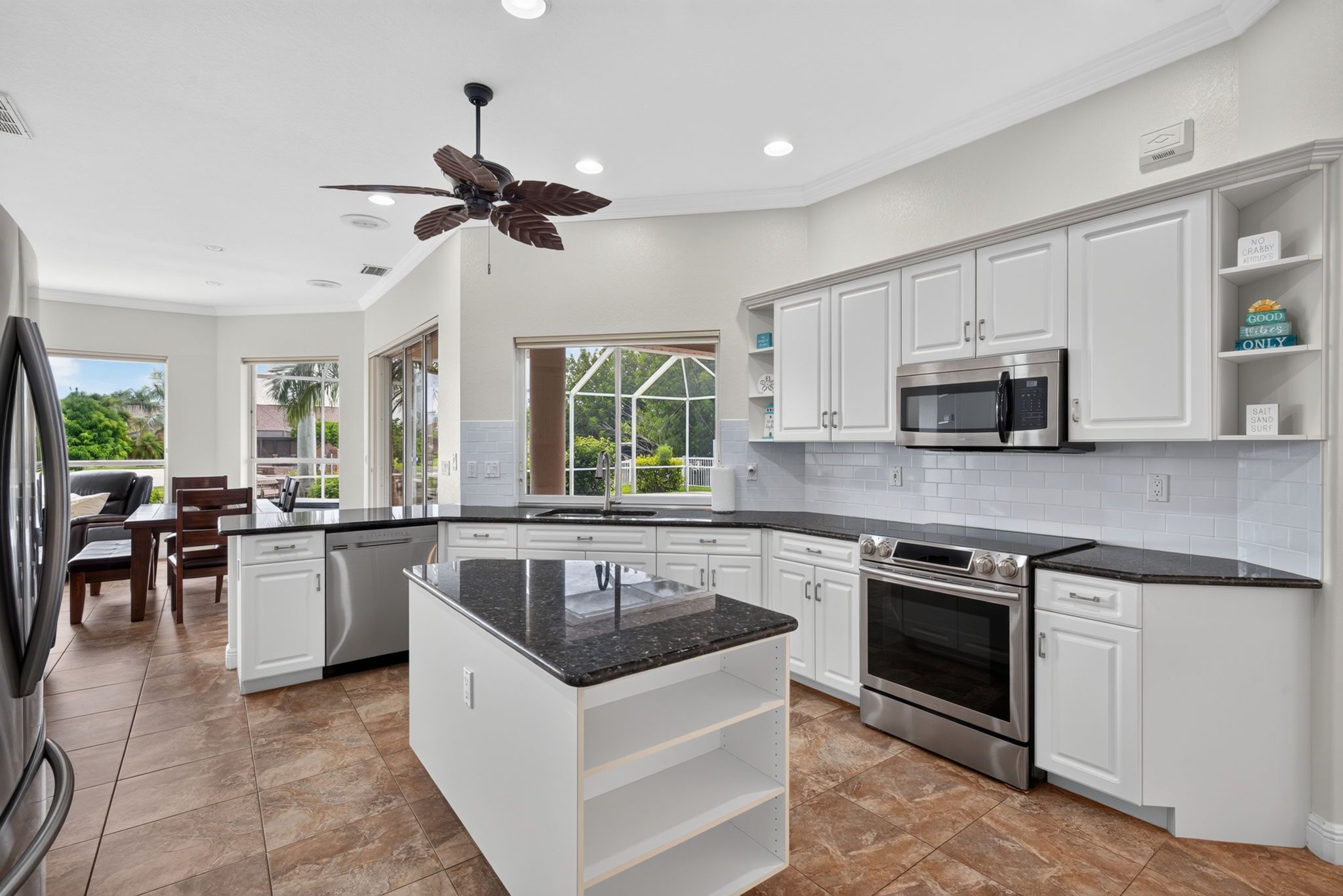 A modern kitchen with white cabinetry, a central island, stainless steel appliances, and a ceiling fan.
