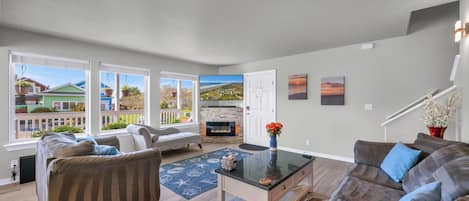 A spacious living room with a fireplace, large windows, and a view of a residential area.
