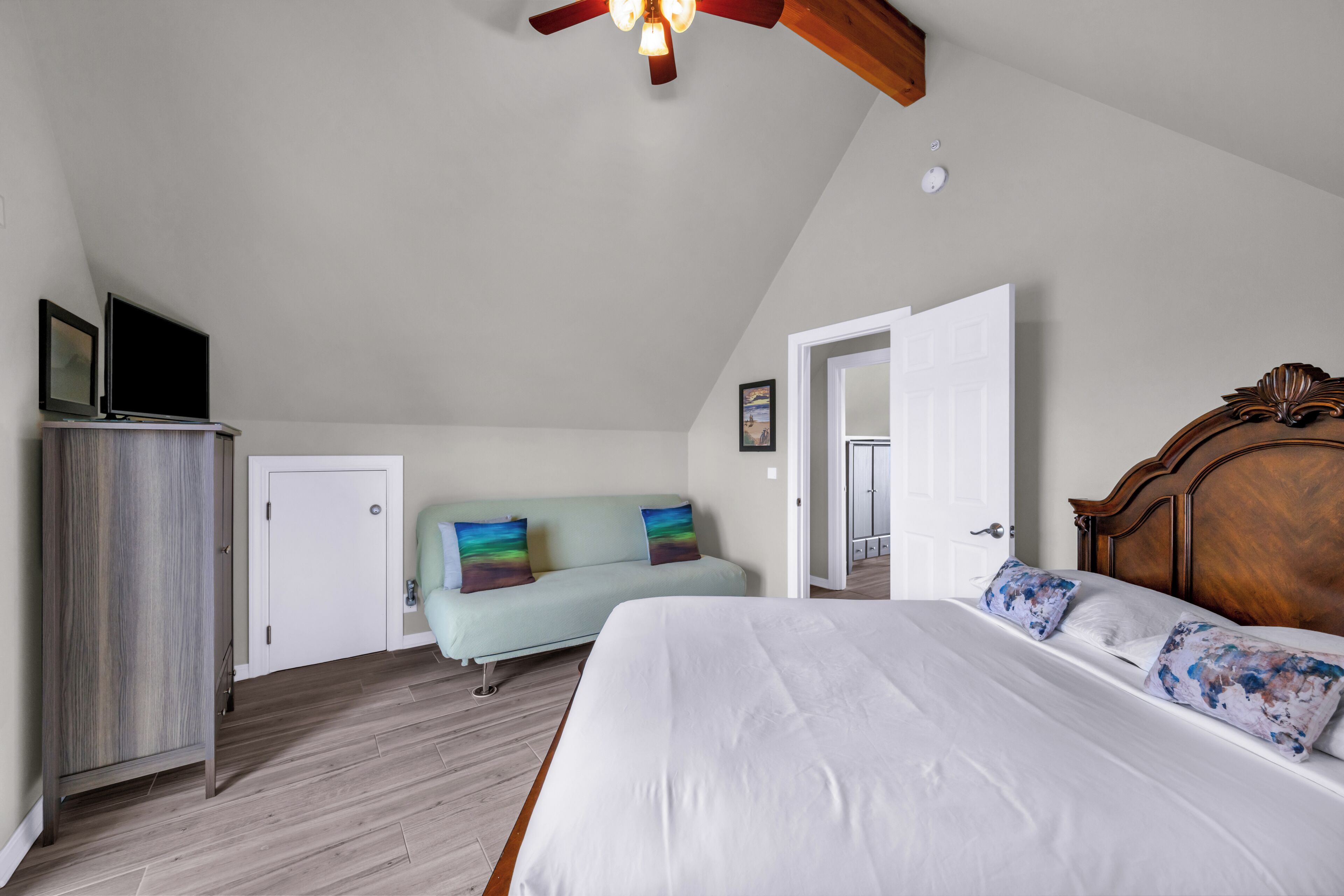 A bedroom with a bed, a sofa, a wardrobe, and a ceiling fan.