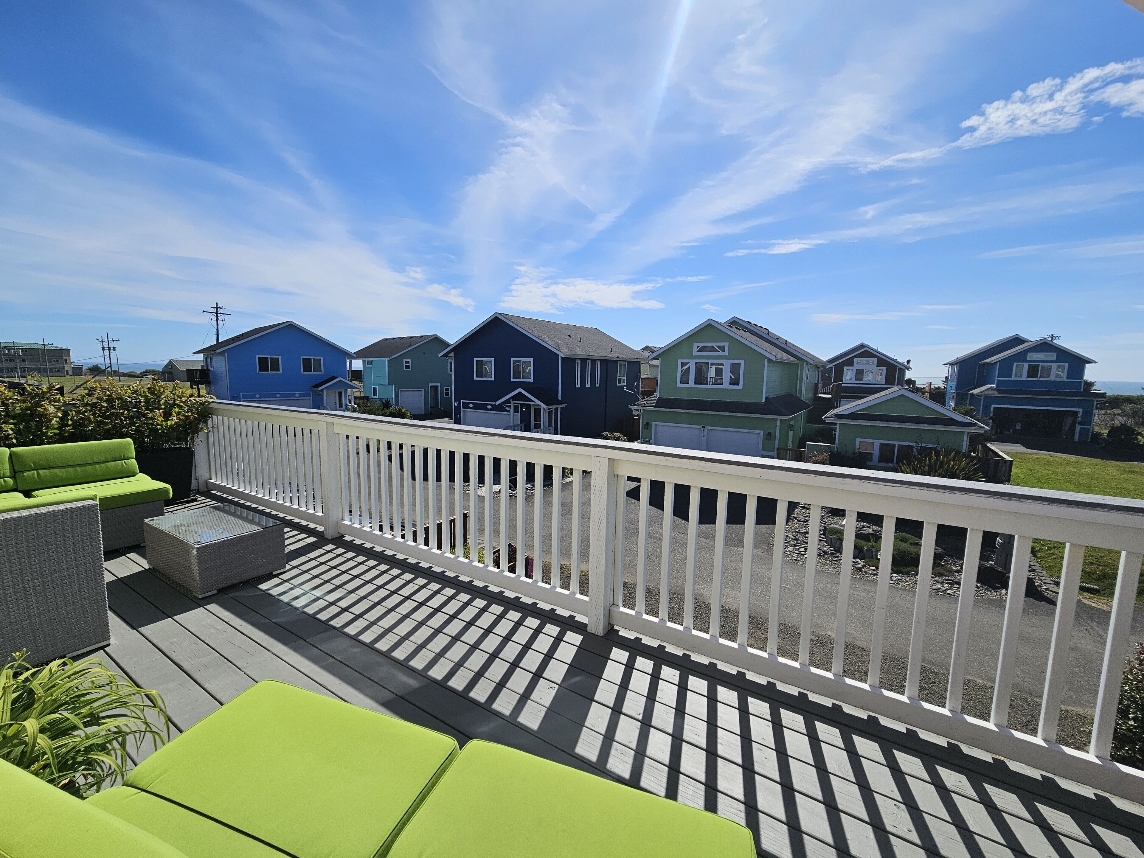 A residential area with a wooden deck, green outdoor furniture, and houses with various architectural styles.