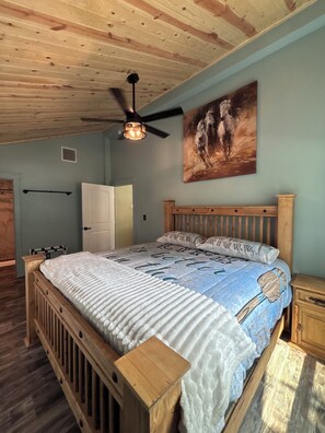 Ein Schlafzimmer mit einem hölzernen Bett, einem Deckenventilator, einem Gemälde an der Wand und einer Tür.
