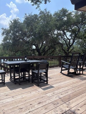 Een terras buiten, met een houten tafel en stoelen, omgeven door bomen.