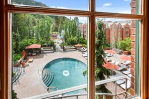 A pool area with lounge chairs and umbrellas, surrounded by greenery and a view of a building with red brick walls. - Luxury 2BR St. Regis Aspen Condo with Concierge & Housekeeping (Aspen)
