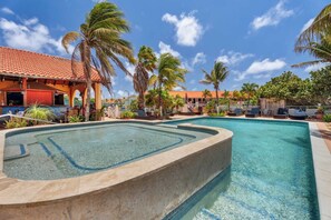 Ein Pool mit Whirlpool, umgeben von Palmen und Liegestühlen.