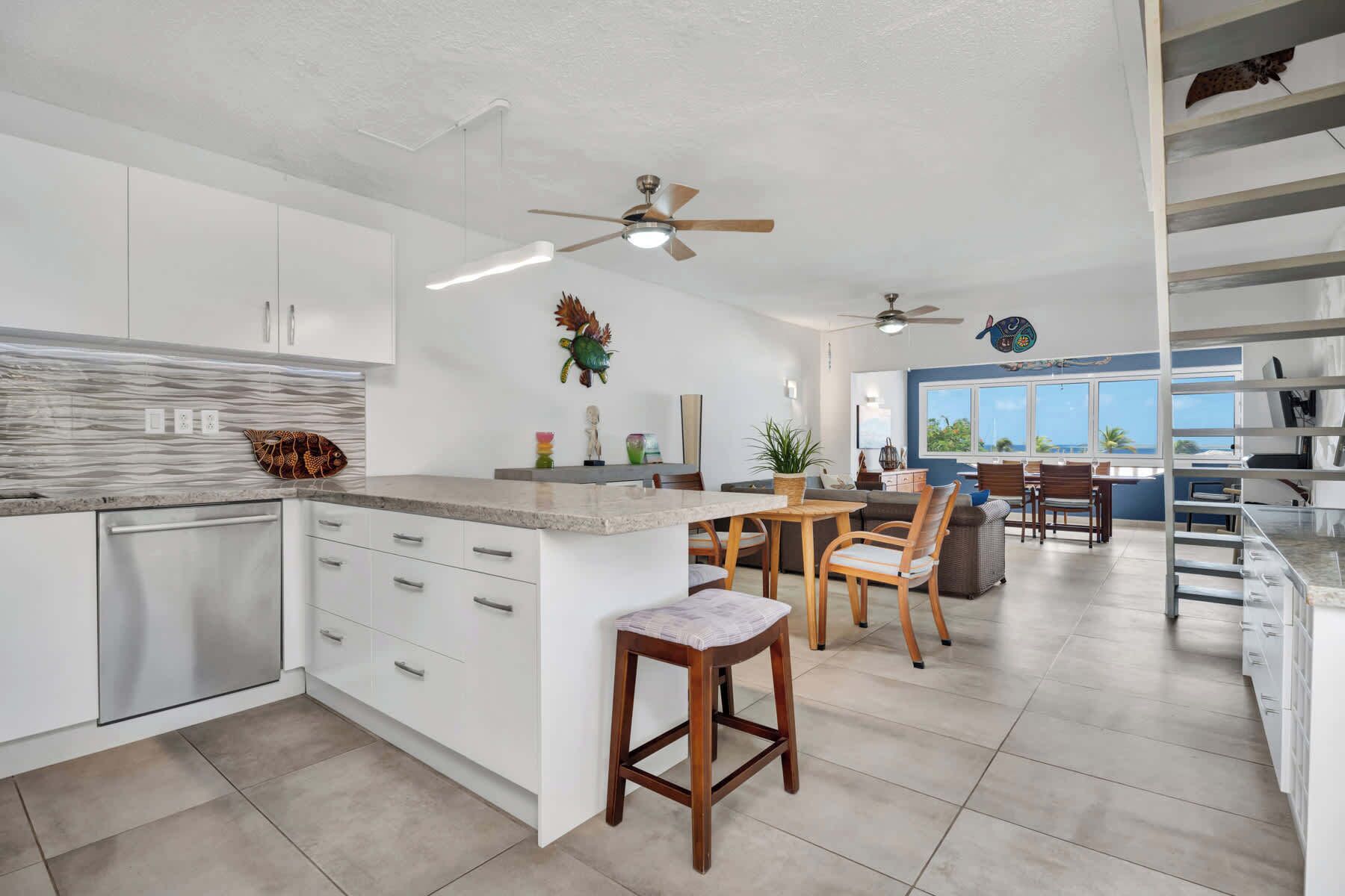 A modern kitchen with white cabinetry, a marble countertop, and a dining area with wooden chairs and a table.