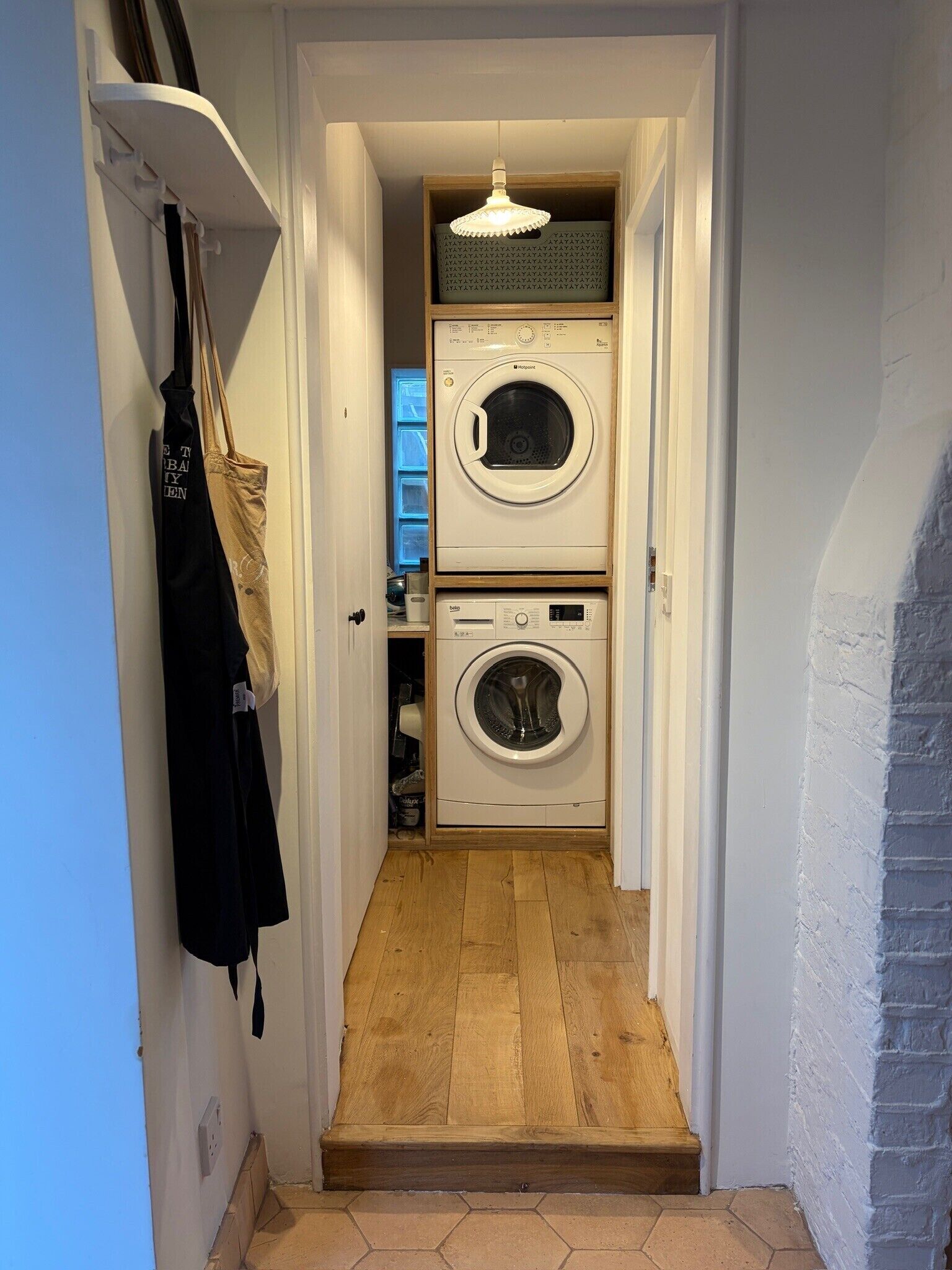 A laundry room with two stacked washing machines, a hanging rack with clothes, and a wooden floor.