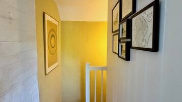 A hallway with a white railing, wooden flooring, and framed artwork on the wall.