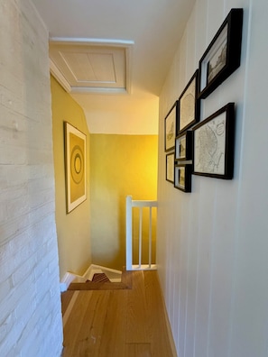 A hallway with a white railing, wooden flooring, and framed artwork on the wall.