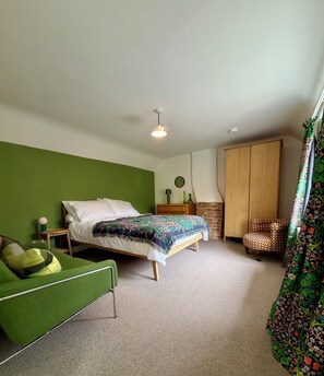 Quarto com cama, cadeira verde, guarda-roupa de madeira e cortina estampada.