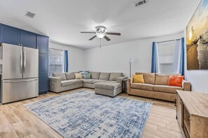 A modern living room with a sectional sofa, a smaller sofa, a wooden coffee table, a ceiling fan, and a large window with curtains. - Pool Retreat | Near USSSA | Beach & Launches (Rockledge)