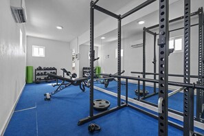 Un gimnasio con equipo de levantamiento de pesas, alfombra azul y un espejo que refleja el equipo.
