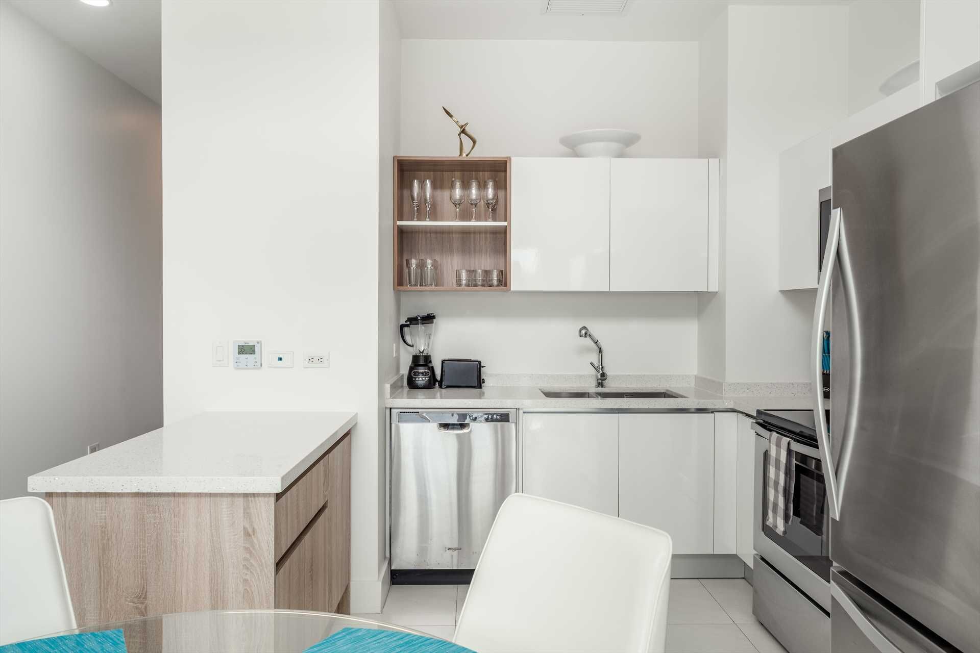 Une cuisine moderne avec des meubles blancs, un réfrigérateur en acier inoxydable, un lave-vaisselle et un plan de travail doté d’un mixeur.